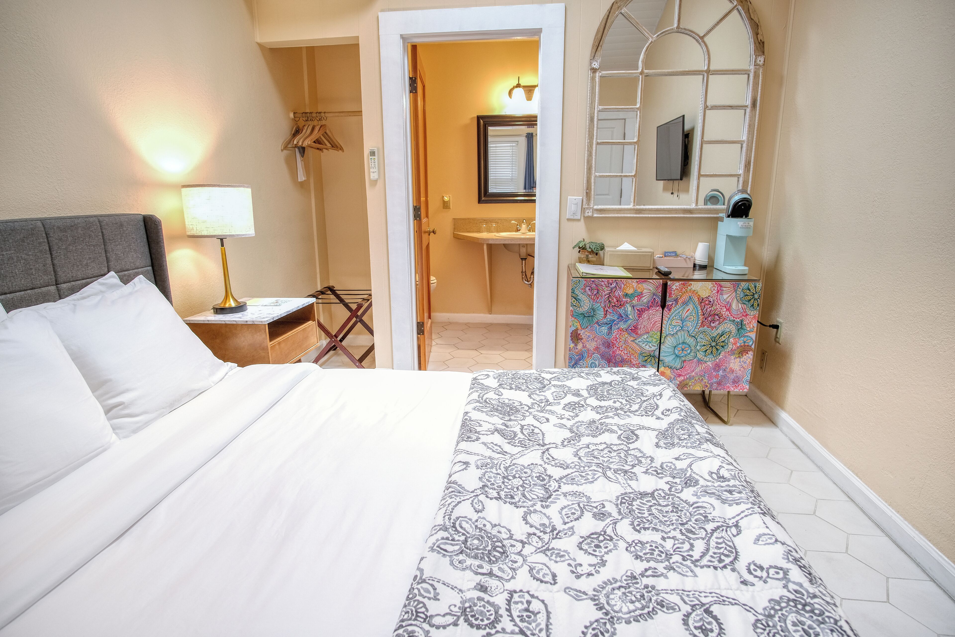 A hotel room with a bed, bedside table, lamp, and a bathroom visible through an open door.