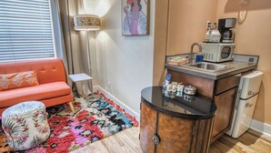 A compact living space with a kitchenette, a sofa, a coffee maker, and a small refrigerator. - Palm Cottages (Ashland)