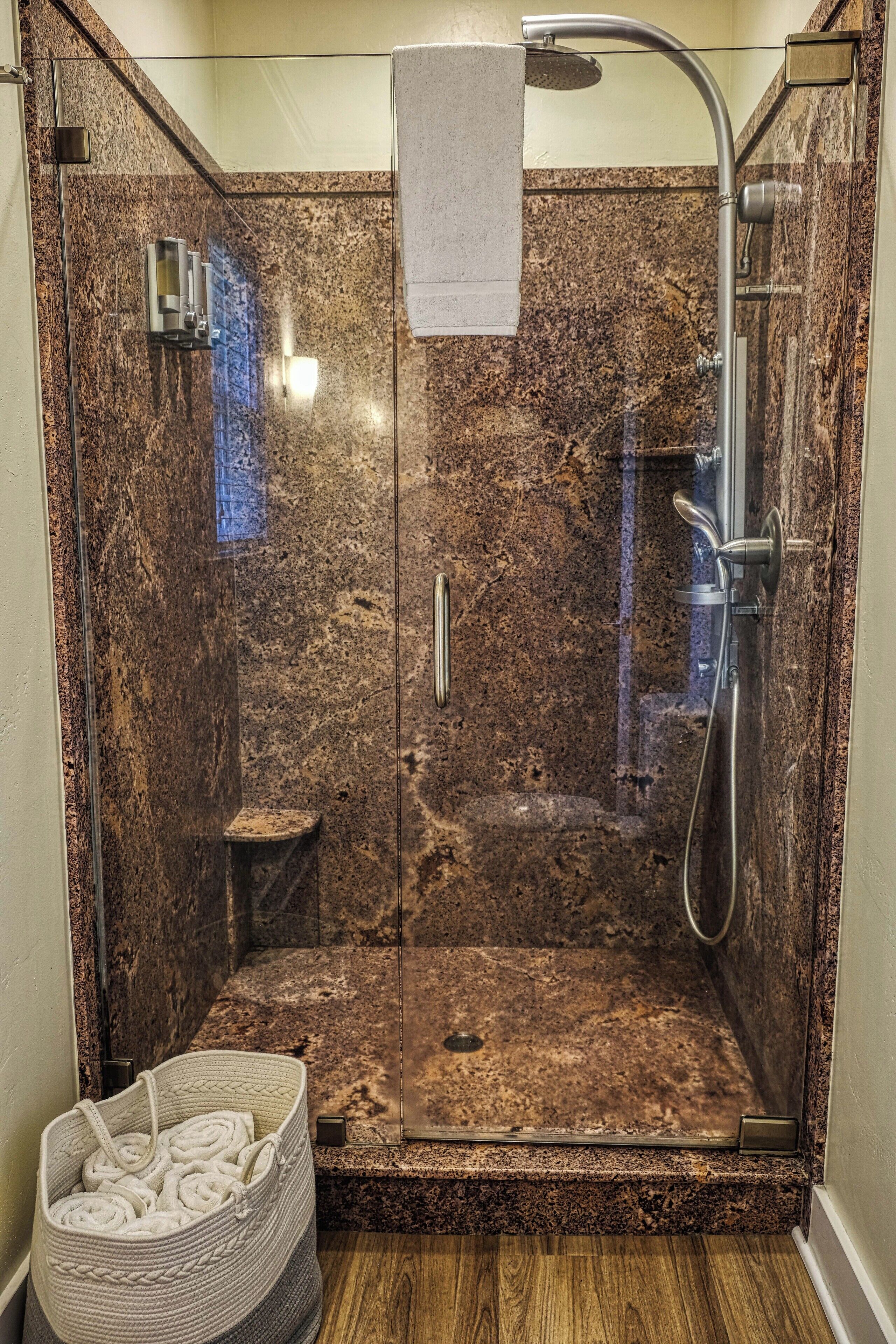Ducha con cerramiento de vidrio, pared de granito, cabezal de ducha manual y perchero.