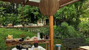 Ein Essbereich im Freien mit einem langen Holztisch, gedeckt für eine Mahlzeit, umgeben von üppigem Grün.