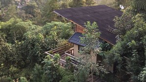 Ein traditionelles japanisches Haus mit einem Ziegeldach, umgeben von üppiger Vegetation und sanften Hügeln im Hintergrund.