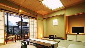 Una habitación japonesa tradicional con suelo de tatami, una mesa baja, un sofá, un televisor y puertas correderas.