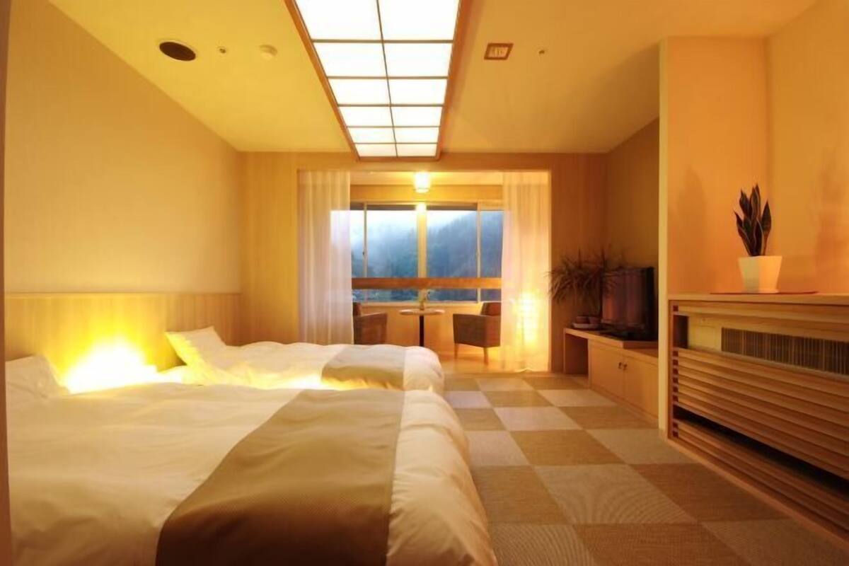 Quarto de hotel com cama, escrivaninha, cadeira, televisão e janela com vista.