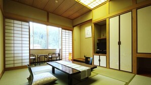 Una habitación con tatami, una mesa baja, cojines, puertas correderas y un televisor.