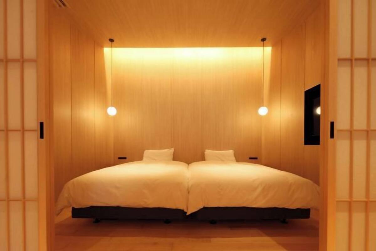 Quarto com duas camas, paredes de madeira e iluminação pendente.