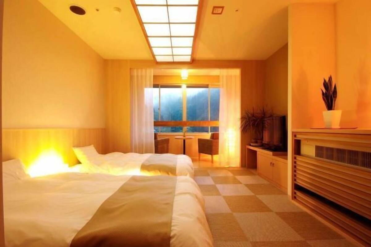 Quarto de hotel com cama, escrivaninha, cadeira, televisão e vista para o exterior.