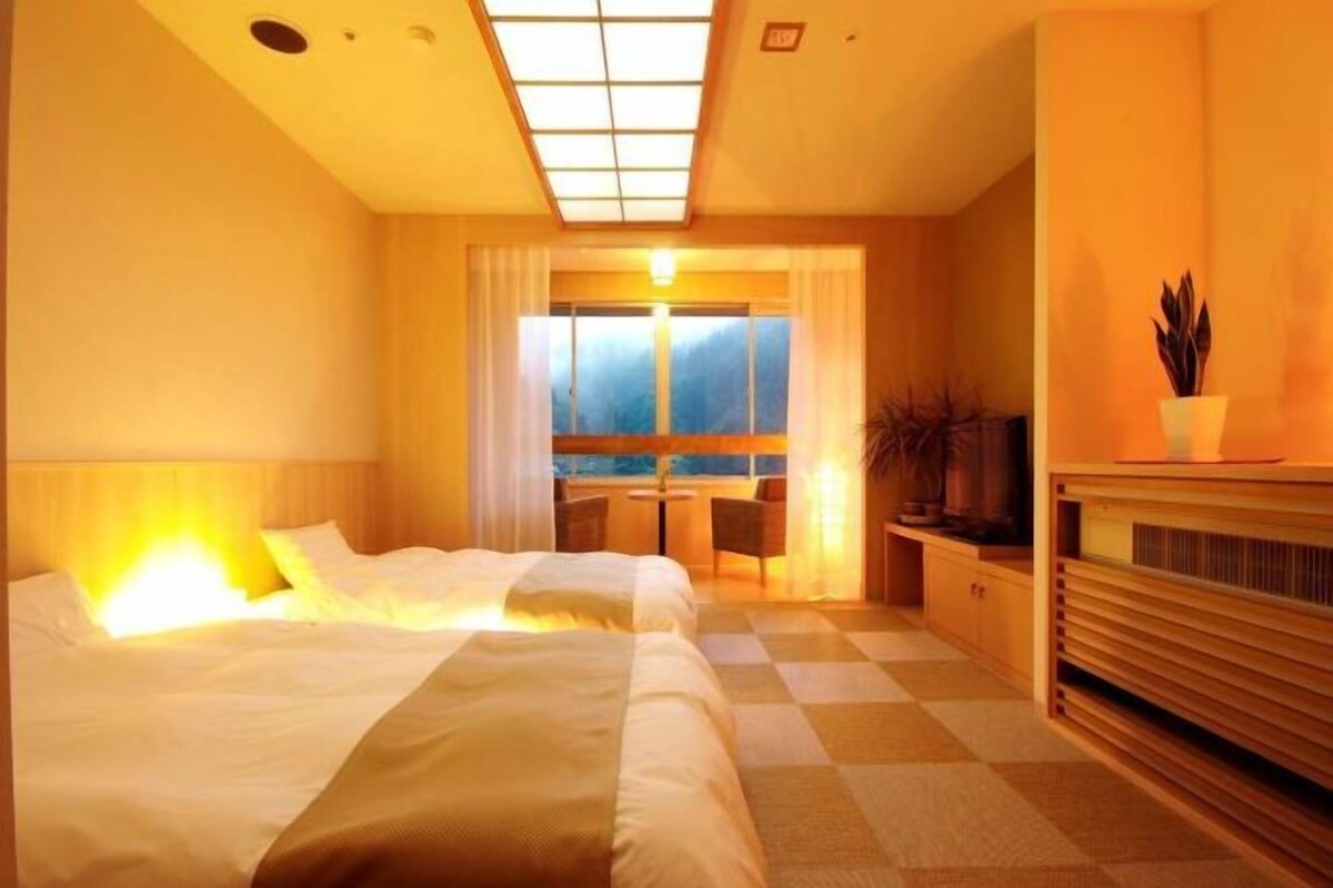 A hotel room with a bed, a desk, a chair, a TV, and a view of the outdoors.