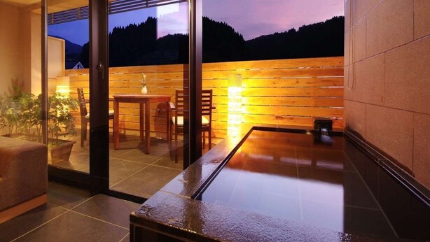 Un interior moderno con una puerta de vidrio que da a un patio, una pared de madera con luz cálida y vistas a un paisaje boscoso.