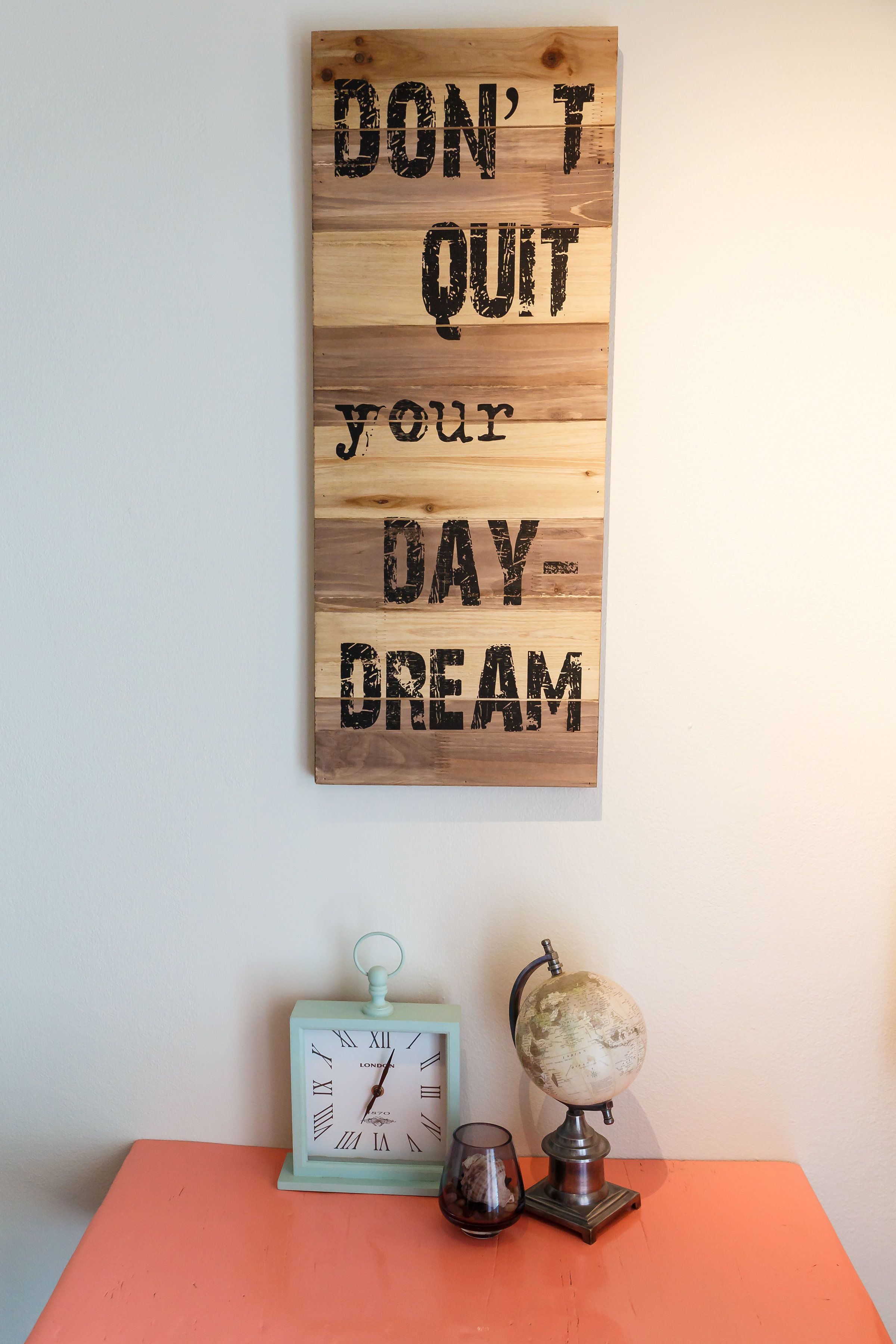 A motivational sign with the text "DON'T QUIT your DAY-DREAM" on a wooden background.