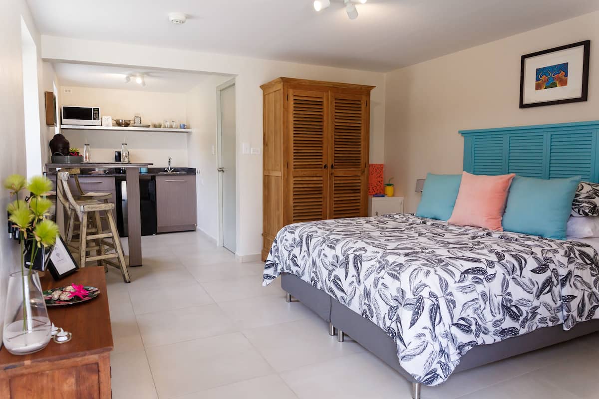 A bedroom with a bed, bedside table, and a view into the kitchen.