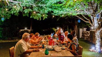 A group of people dining at an outdoor table under a tree, with string lights above.
