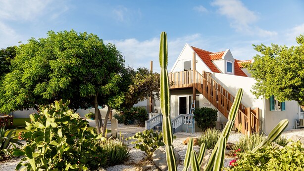 A house with a white exterior, red roof, and a wooden staircase leading to a balcony. - Aruba Boutique Apartments Adults Only (Noord)