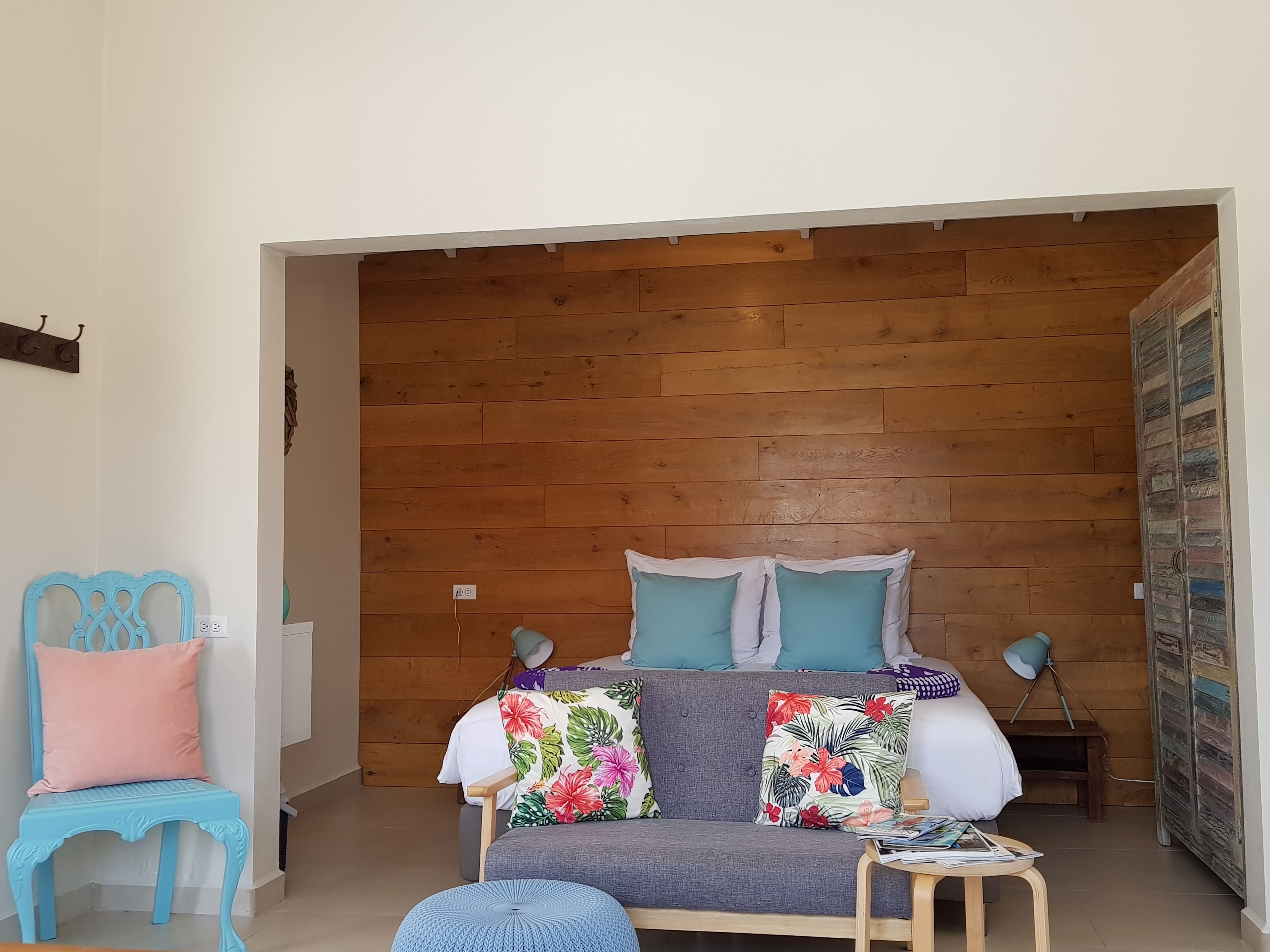 Un salón acogedor con una pared de madera, un sofá gris con cojines estampados, una silla azul y una pequeña mesa de madera.