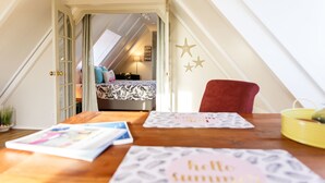 A cozy attic bedroom with a sloped ceiling, a bed with patterned bedding, a red chair, and a table with magazines and a bowl. - Aruba Boutique Apartments Adults Only (Noord)