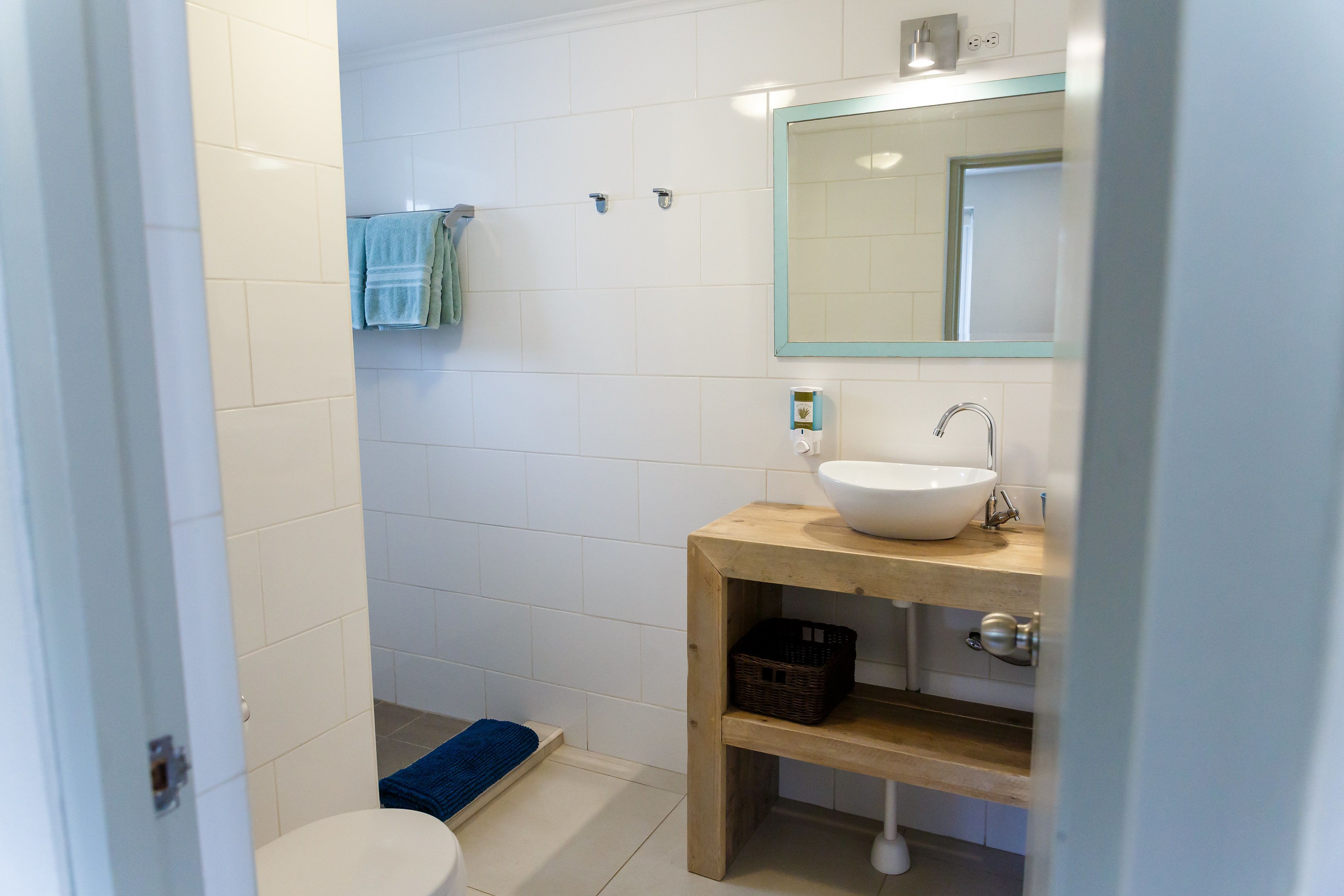 Un baño con inodoro blanco, lavamanos con espejo y felpudo azul.