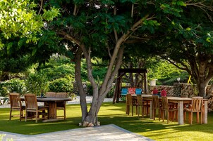Un área de comedor al aire libre con mesas y sillas de madera, rodeada de abundante vegetación y árboles.