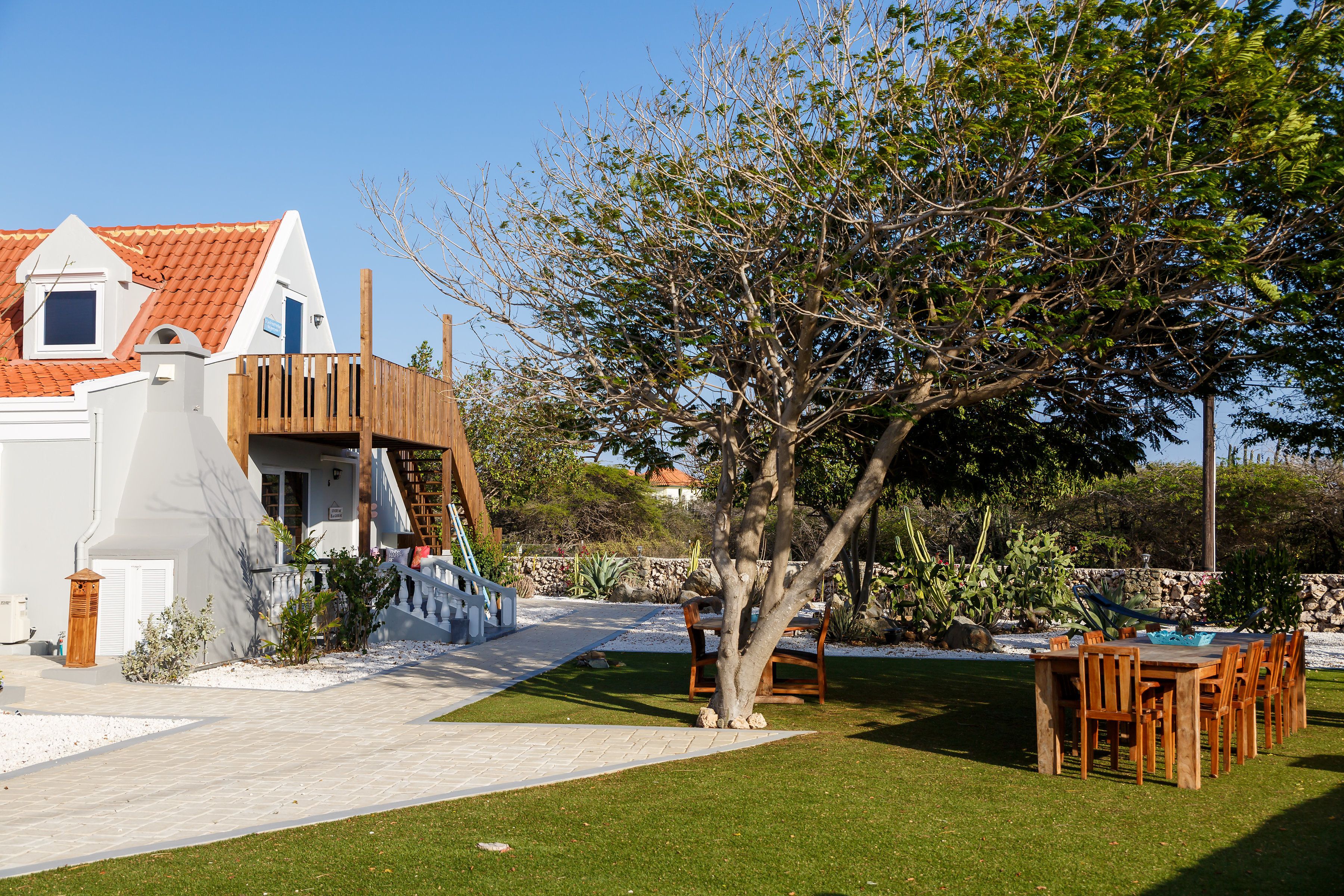 Una casa con fachada blanca, techo de tejas rojas y terraza de madera.