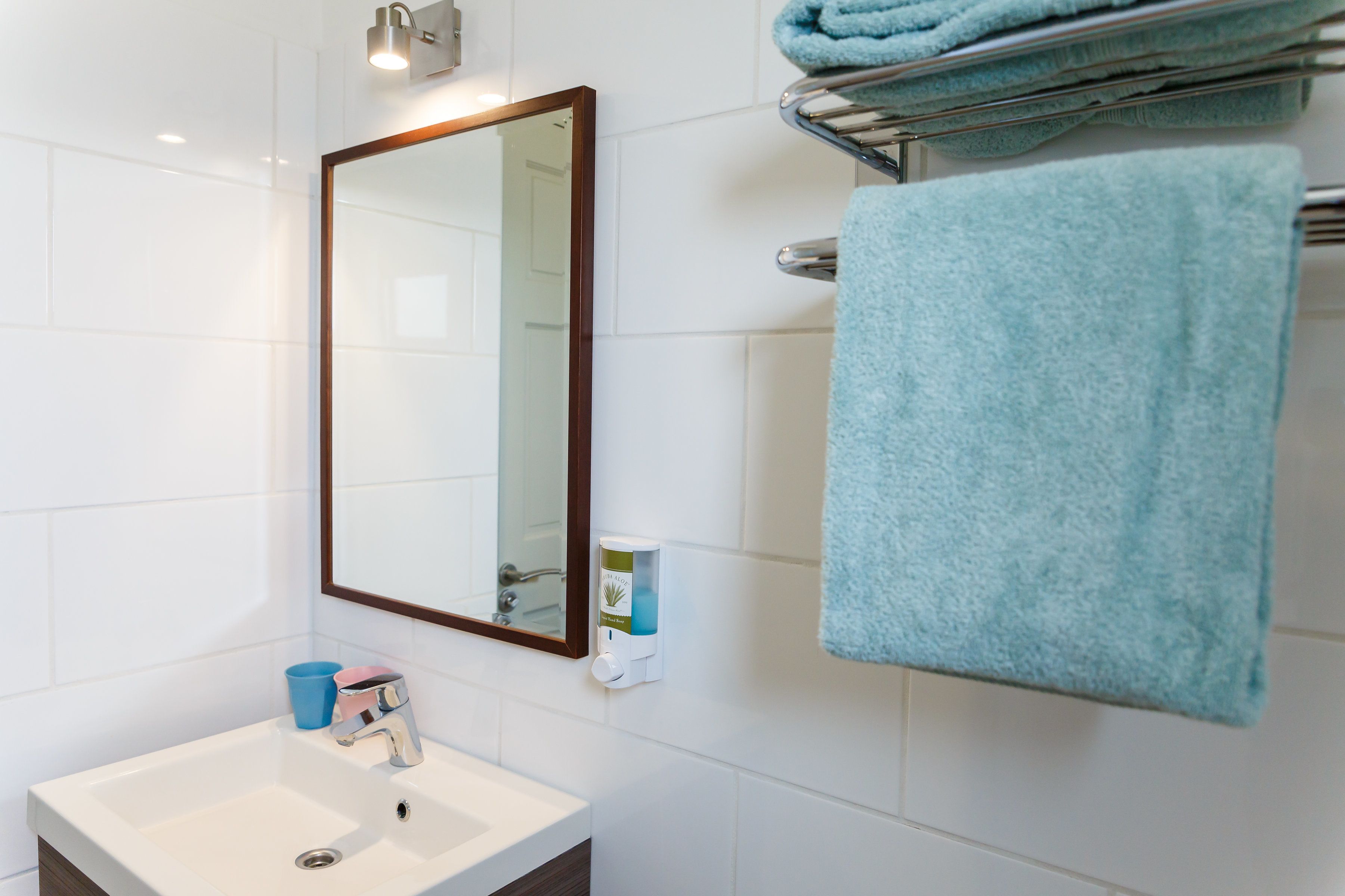 Uma casa de banho com uma pia branca, um espelho, um porta-toalhas com uma toalha azul e um dispensador de sabonete.