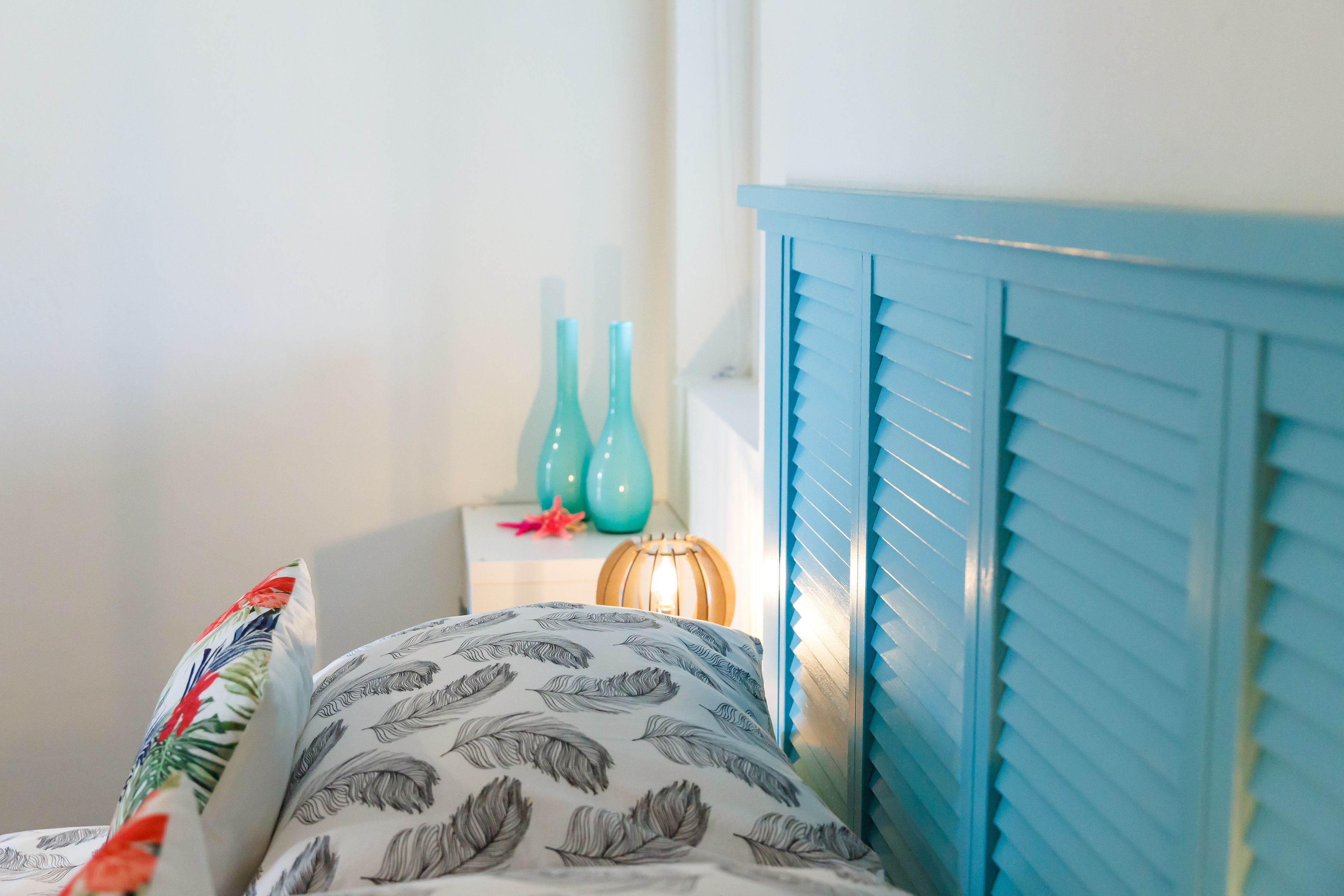 Une chambre à coucher avec un lit, une table de chevet ornée de vases décoratifs et une tête de lit bleue.
