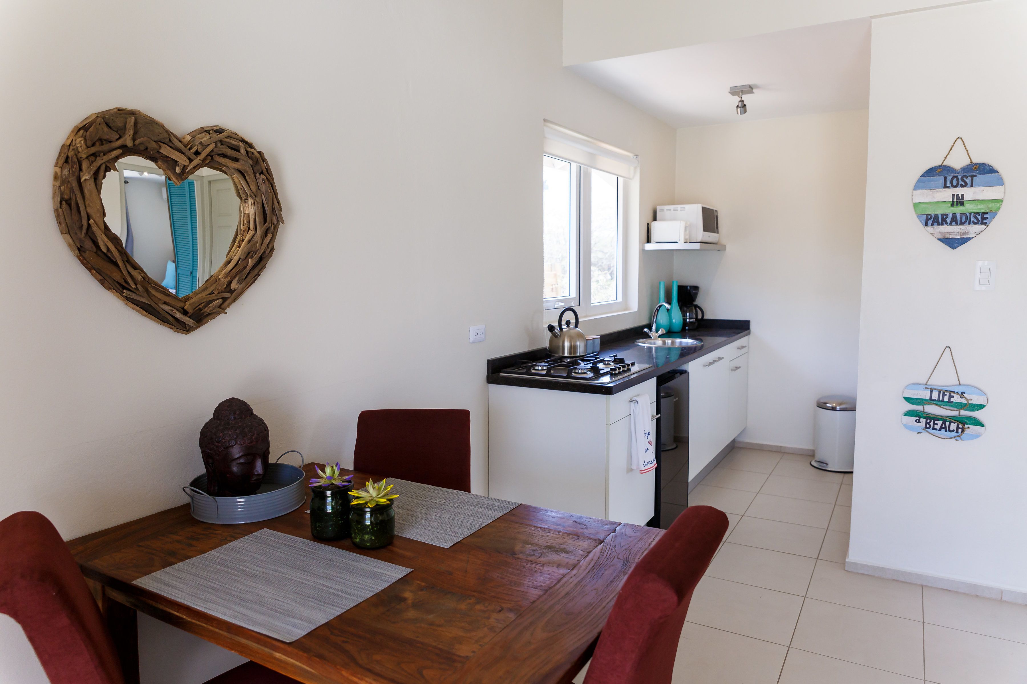 A compact kitchen with a heart-shaped mirror, a Buddha statue, and a small dining table with chairs.