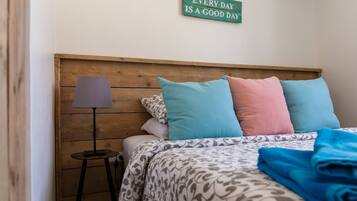 Un dormitorio con cabecera de madera, cama con ropa de cama estampada y una lámpara de noche.
