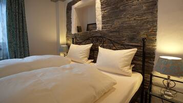 A double bed with white linens, a stone wall, and a lamp on a bedside table.