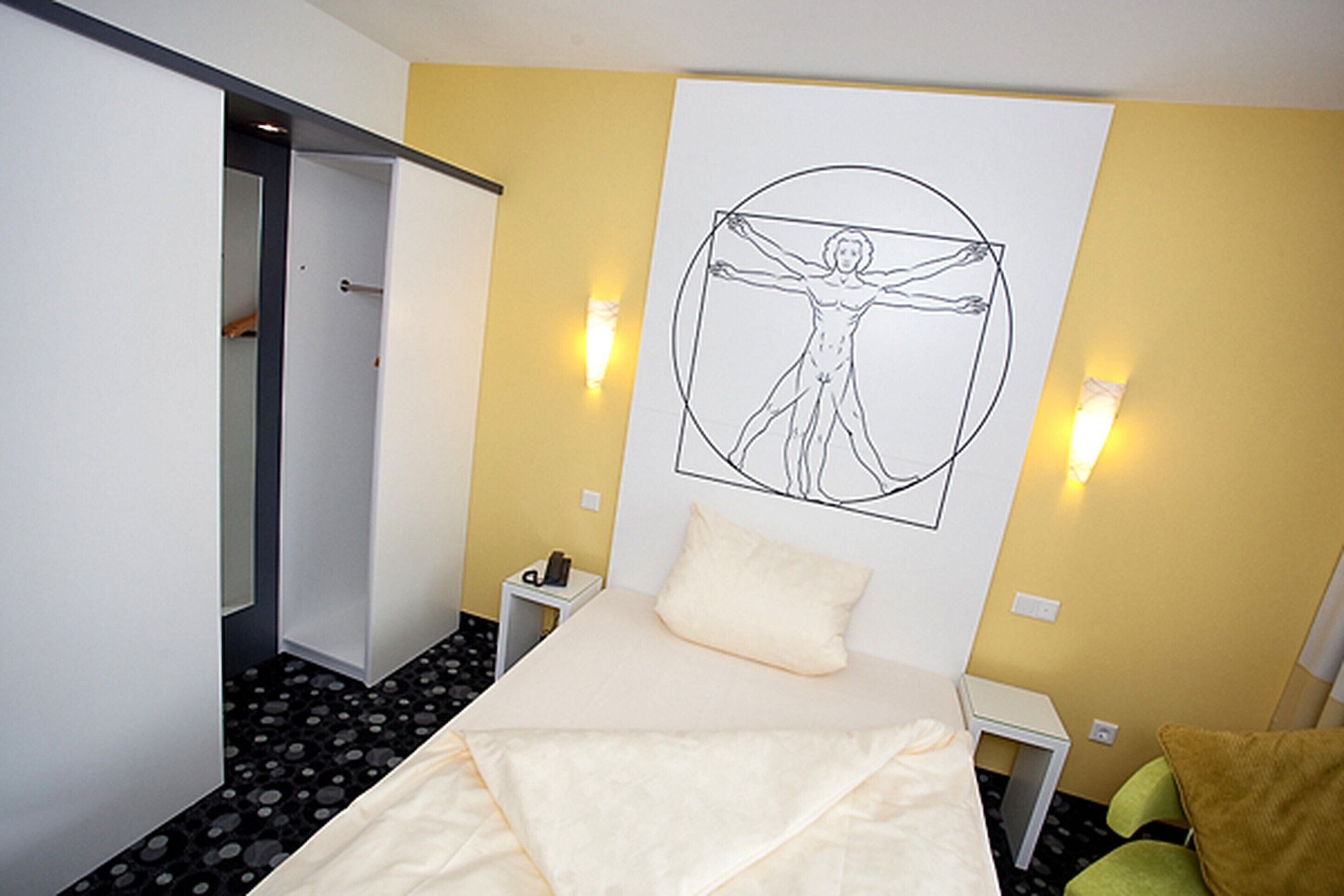 A hotel room with a bed, a wall-mounted artwork of a human figure, bedside tables, and a door leading to a hallway.