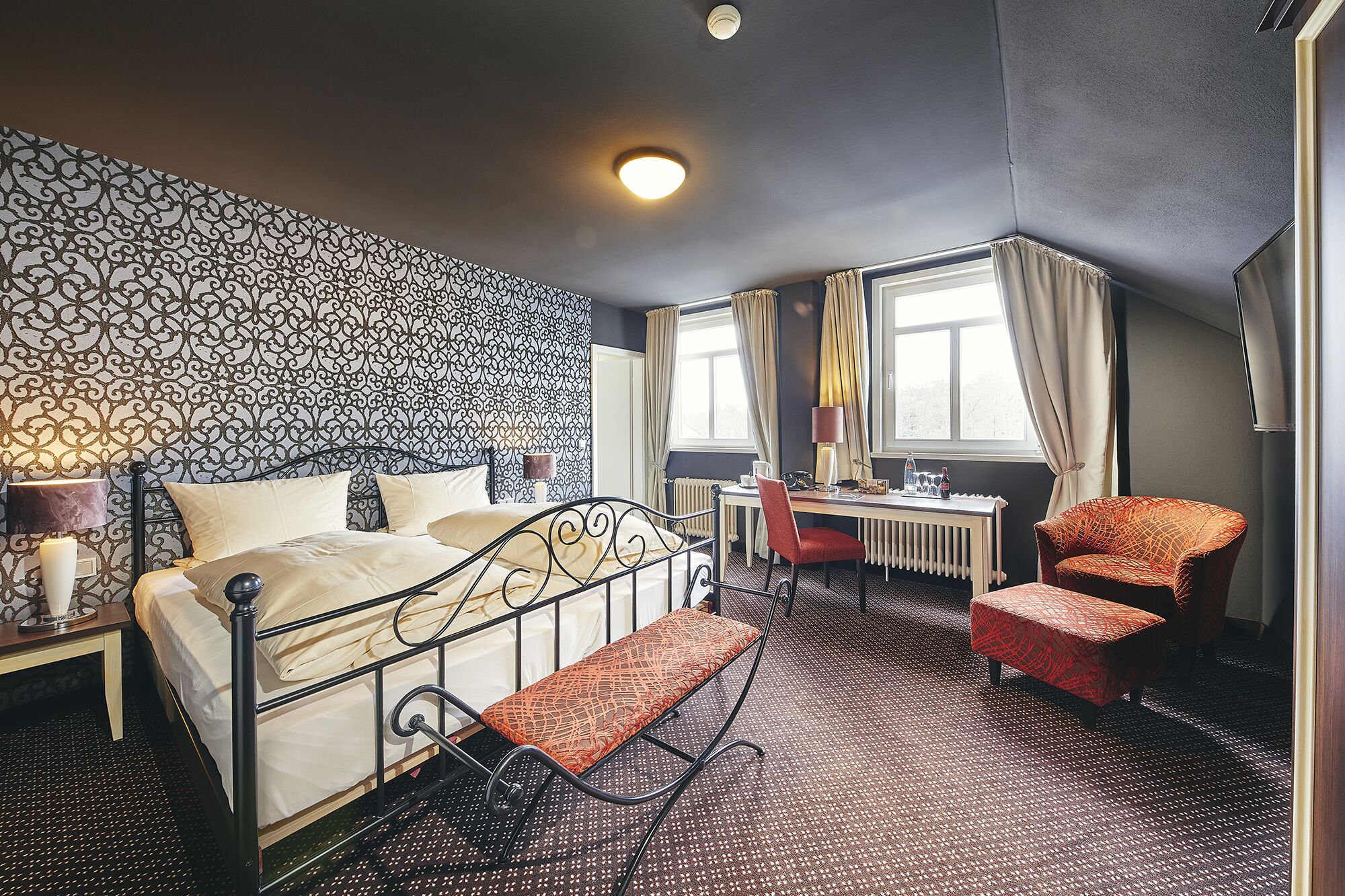 A hotel room with a bed, a desk, a chair, and a radiator.