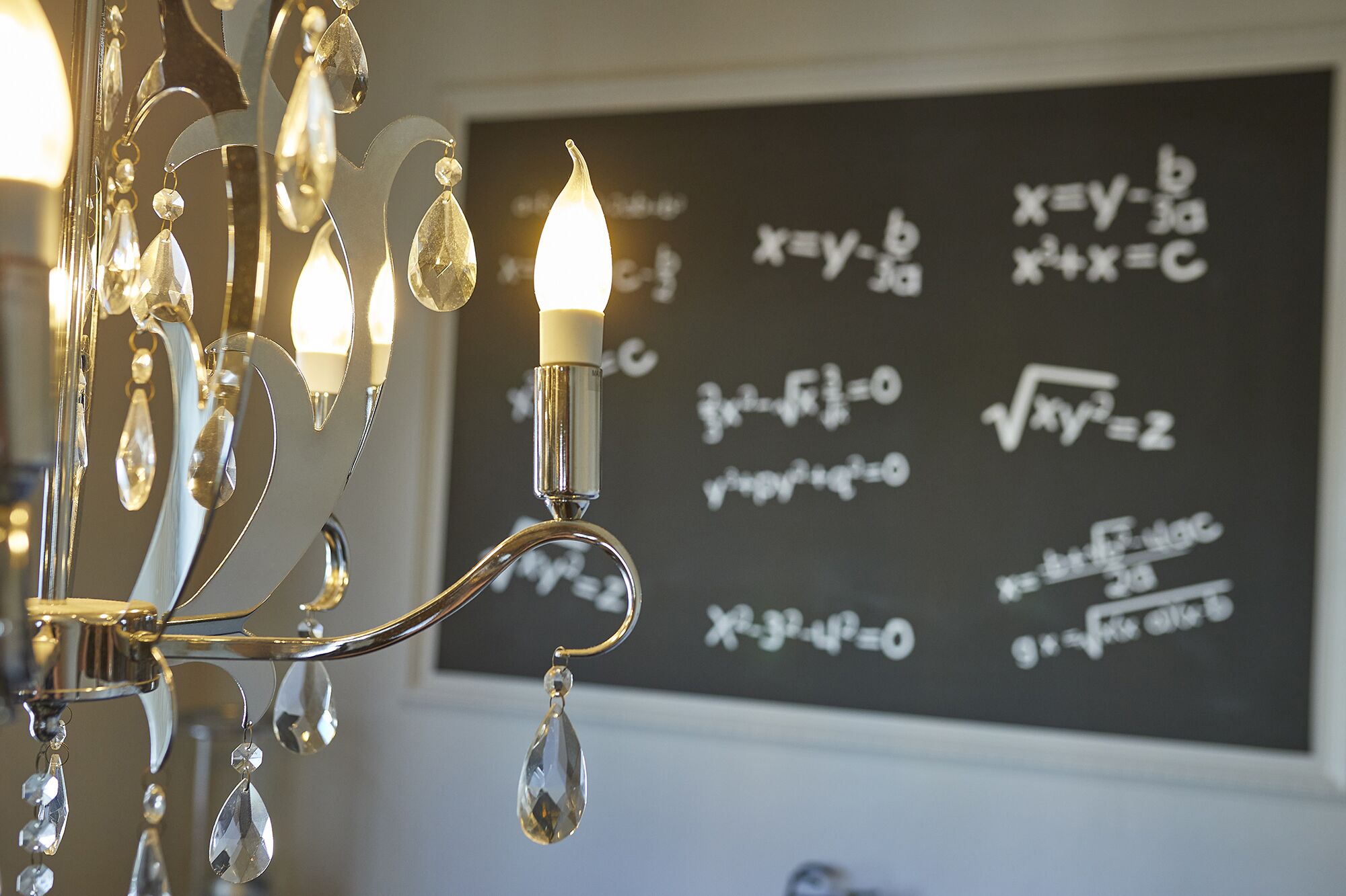 Un candelabro con adornos de cristal frente a una pizarra con ecuaciones matemáticas.