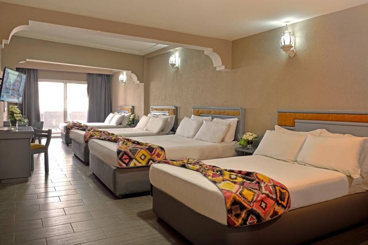Une chambre d’hôtel avec trois lits, un bureau et une télévision.