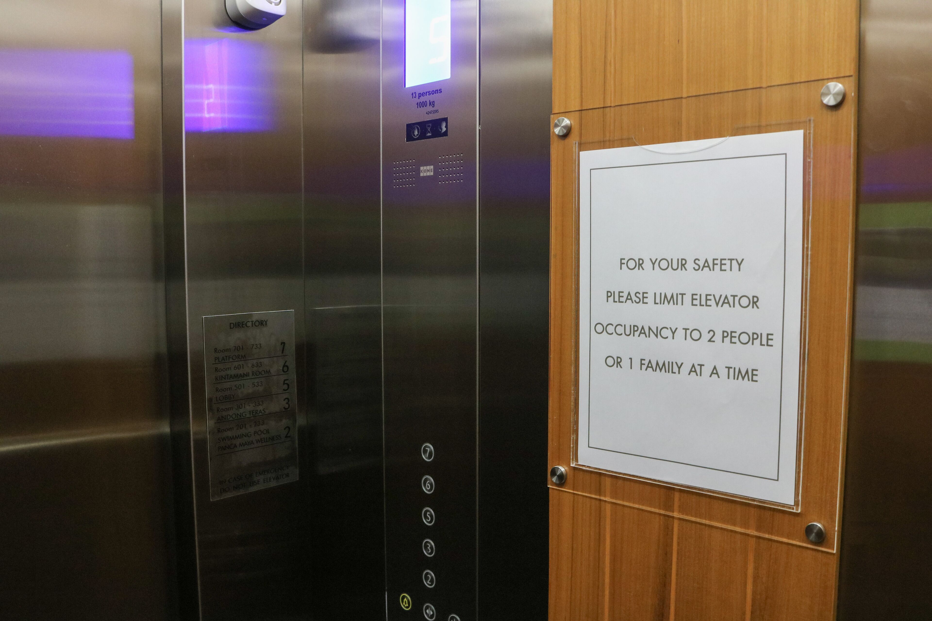 Intérieur d’un ascenseur avec une affiche indiquant qu’il est interdit de dépasser un maximum de deux personnes ou une seule famille à la fois, pour des raisons de sécurité.