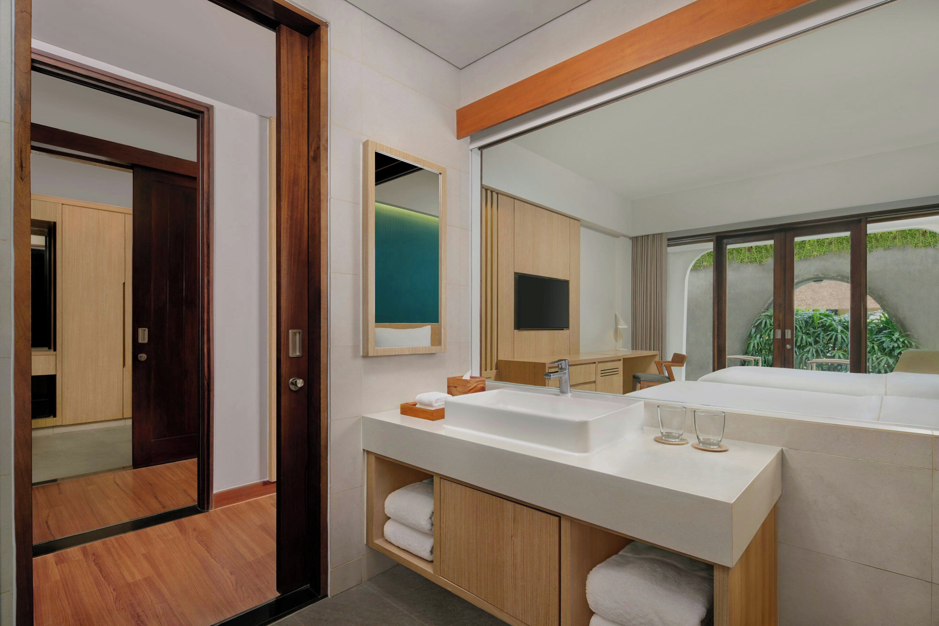 Un baño moderno con un espejo grande, dos lavamanos, armarios de madera y vistas a zonas verdes.