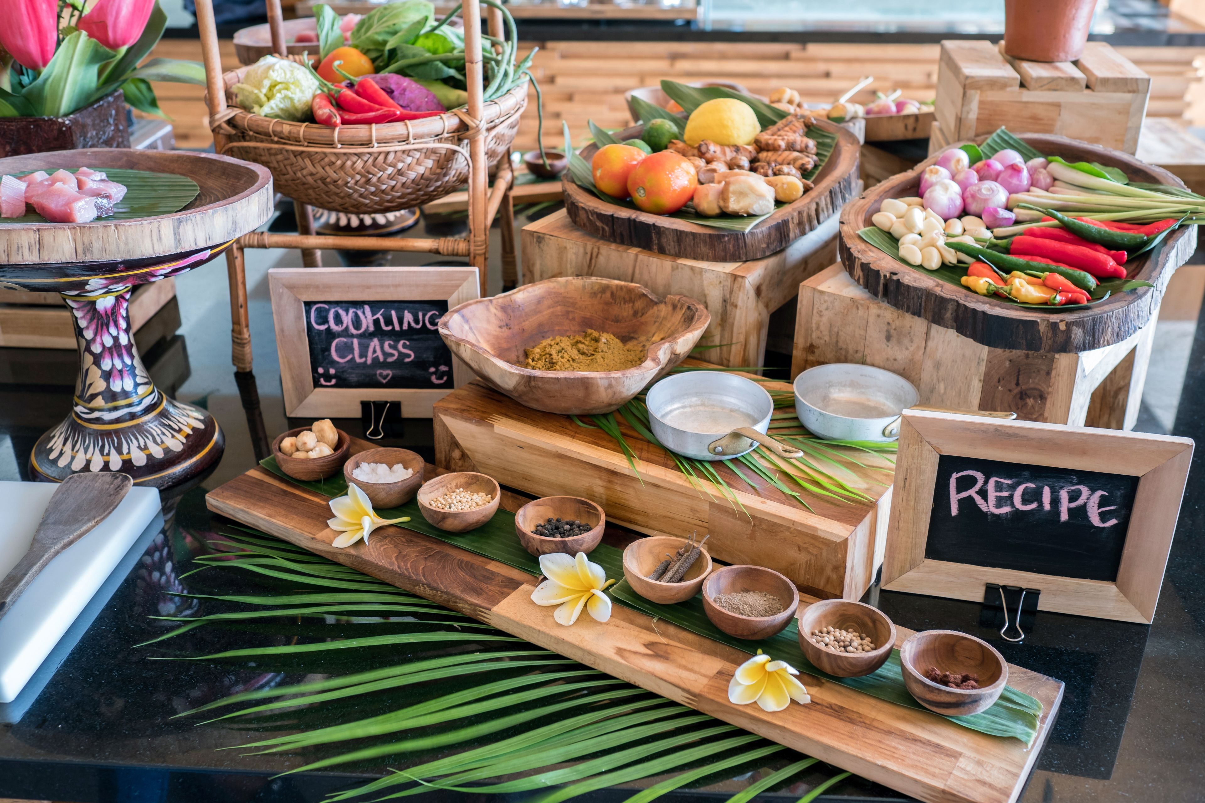 Uma mesa de madeira com várias tigelas contendo especiarias e ingredientes, uma placa com a inscrição 'COOKING CLASS' e outra com a inscrição 'RECIPE'.