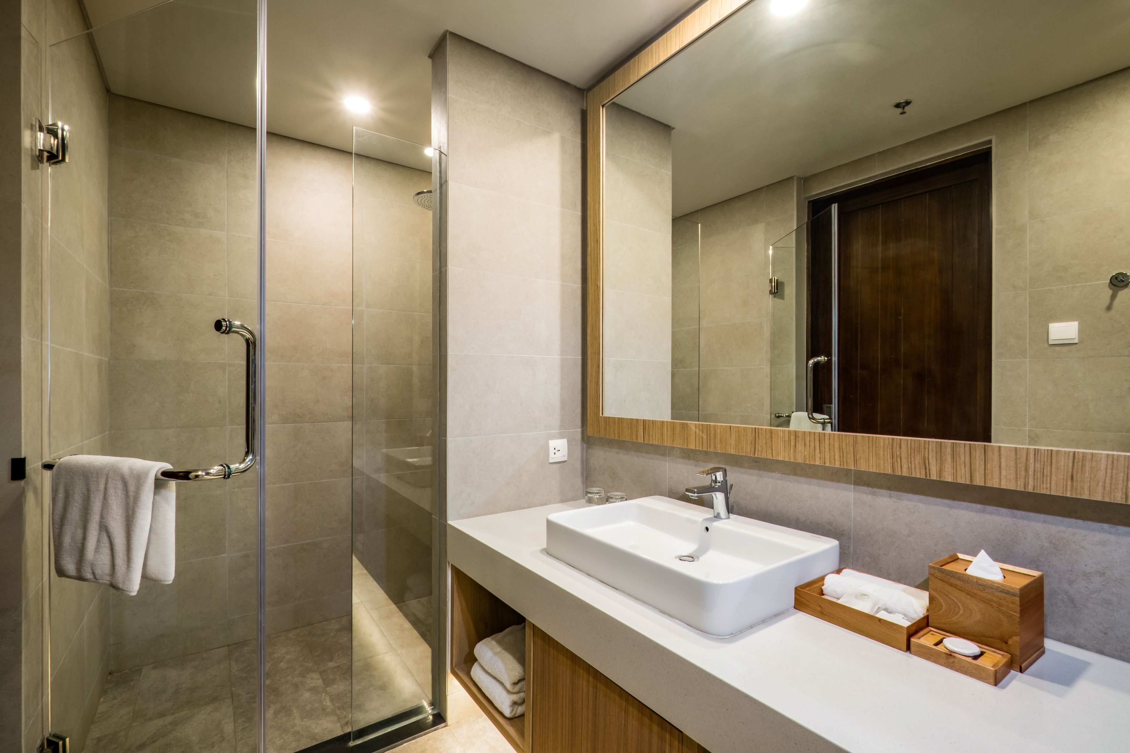 Un baño moderno con ducha envuelta en vidrio, un lavabo blanco y un mueble de tocador de madera.