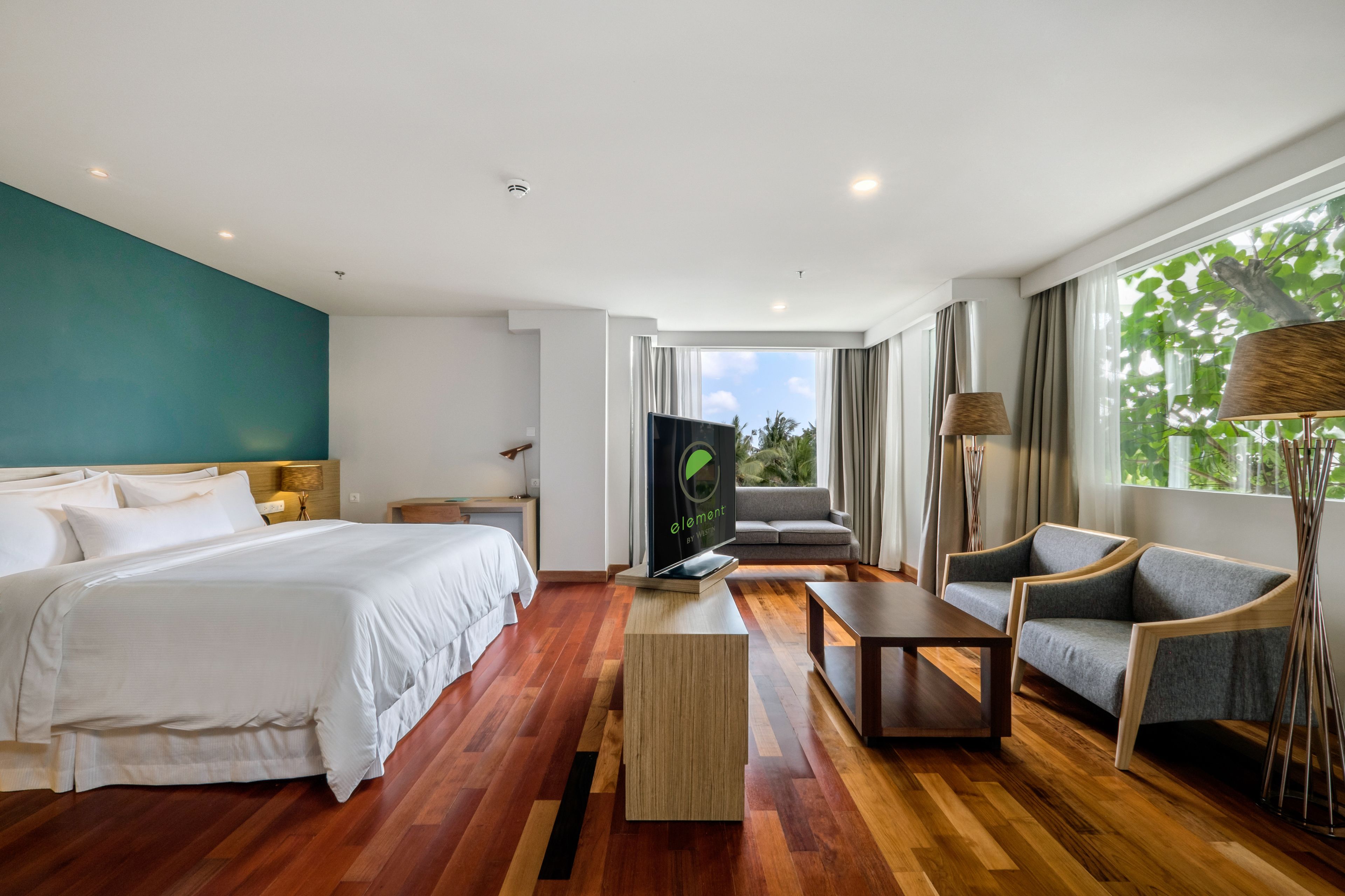 Una habitación de hotel moderna con una cama grande, un sofá, una mesa de centro y un televisor.