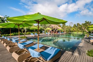 Zona junto a la piscina con sillones de descanso y sombrillas verdes.