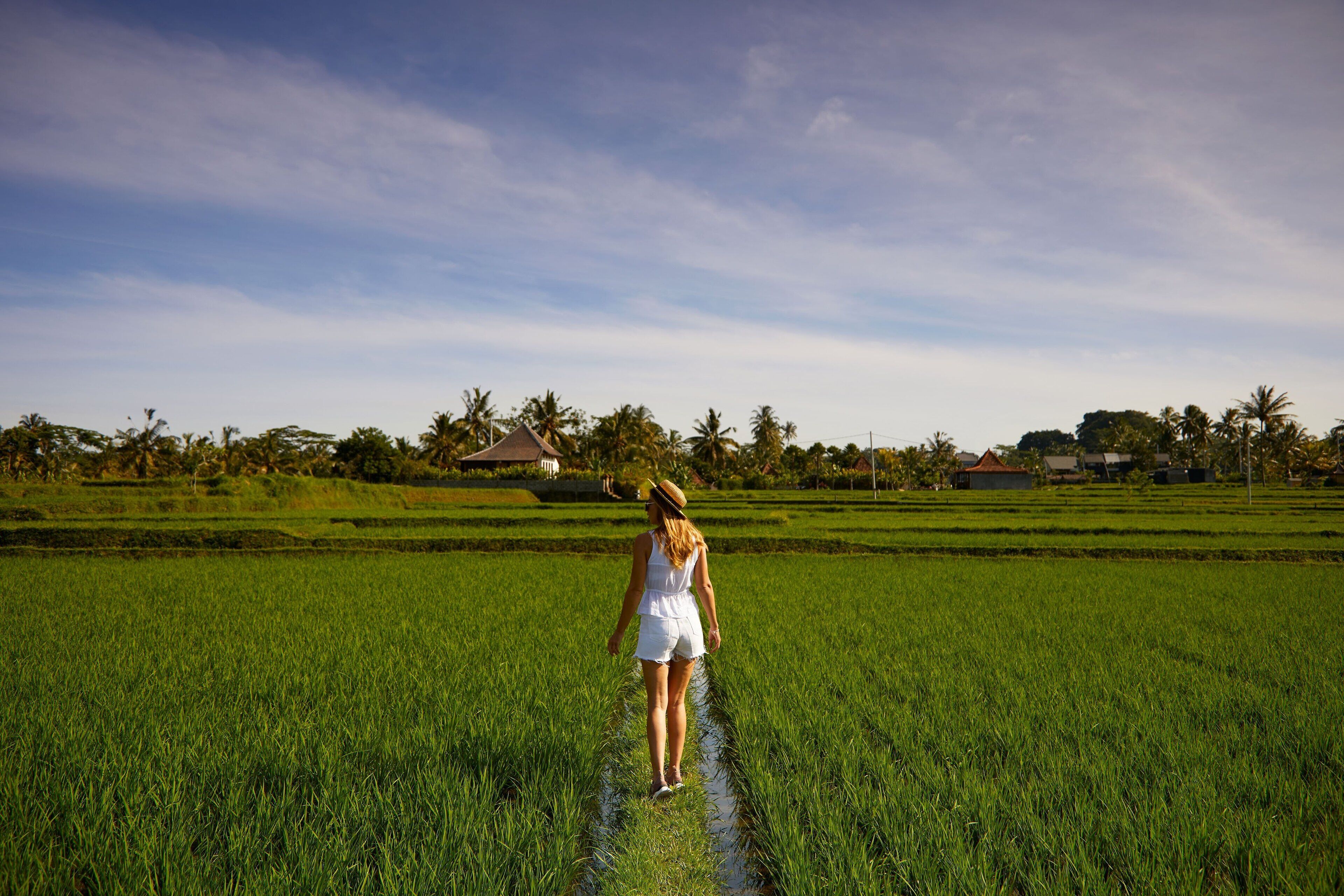 A woman walking through a lush green field with houses in the background.