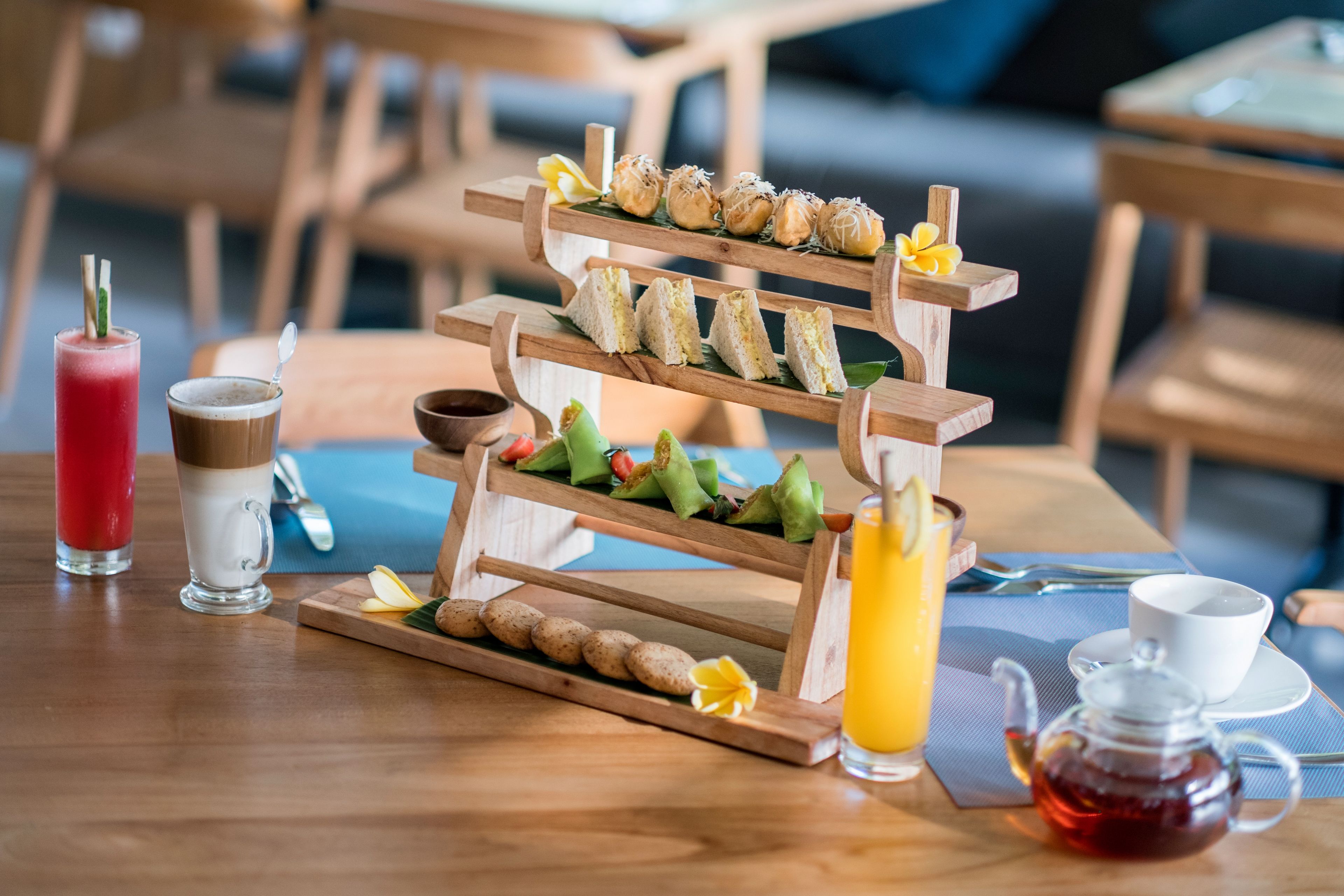 Une table de petit-déjeuner avec un présentoir en bois à plusieurs niveaux, sur lequel sont disposés divers en-cas et une théière.
