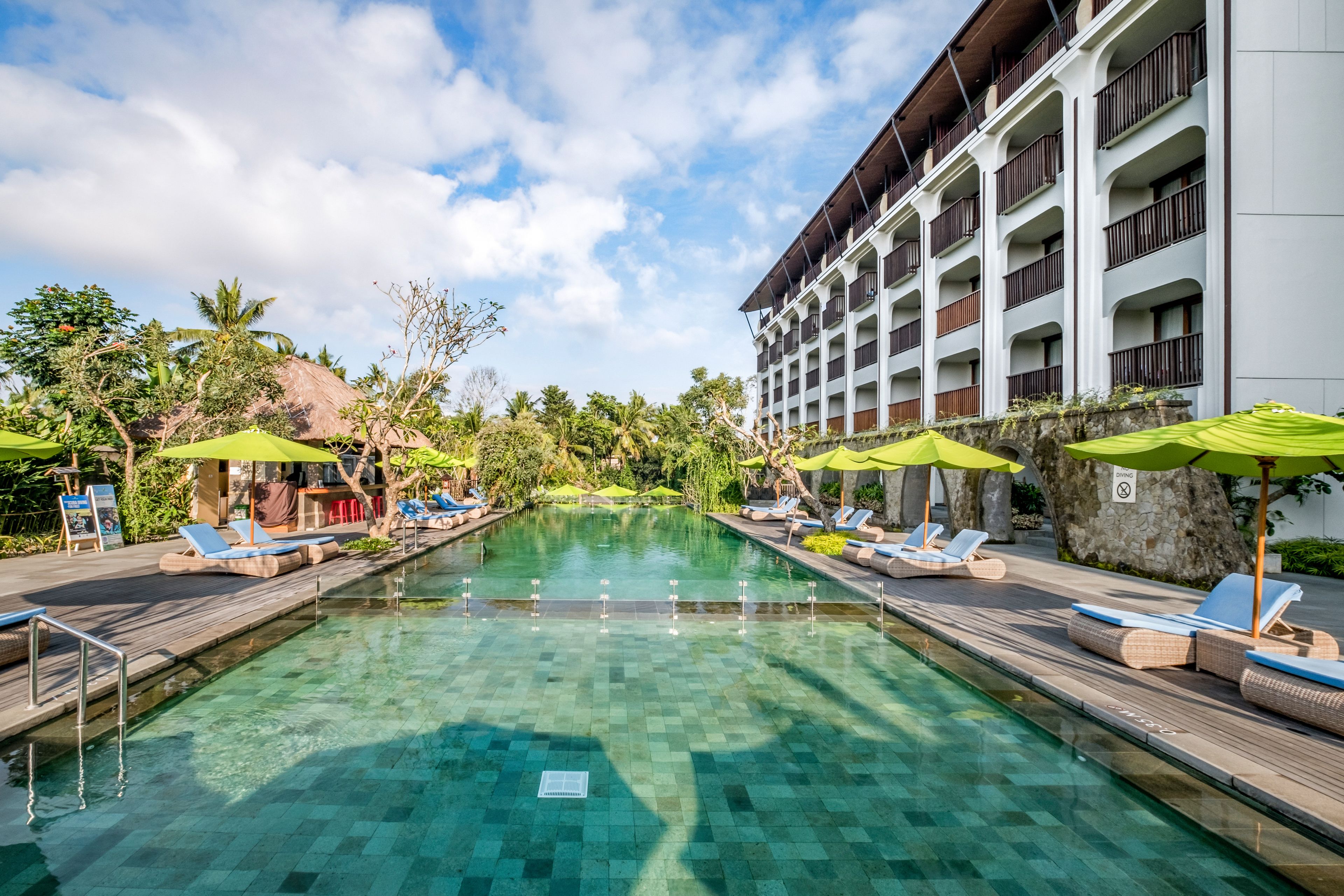 A pool area with lounge chairs and umbrellas, surrounded by a building with balconies.