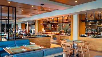 A modern restaurant with wooden accents, blue seating, and a kitchen area visible in the background.