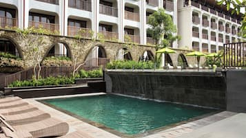 A hotel pool area with lounge chairs, a stone bridge, and a waterfall.
