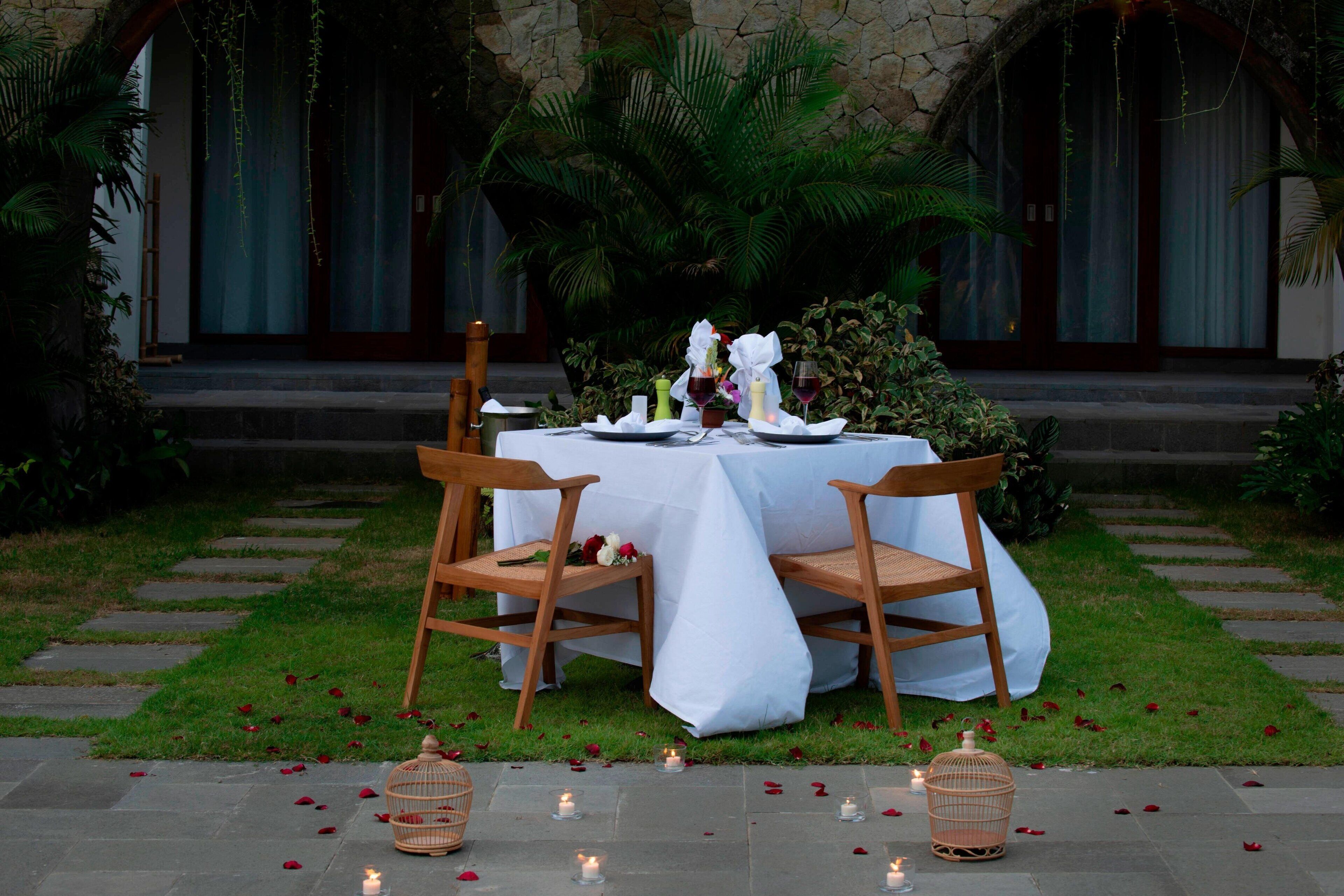 An outdoor dining setup with a table set for two, surrounded by greenery and stone steps.