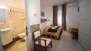 A hotel room with a bed, a chair, a bedside table, a nightstand, a lamp, a mirror, a bathroom with a sink, a toilet, and a shower. - Vebis Guesthouse (Rome)