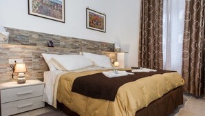 A neatly made bed with a brown and white duvet, a bedside lamp, and a nightstand with a lamp. - Vebis Guesthouse (Rome)