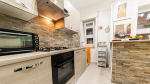A modern kitchen with a built-in microwave, gas stove, oven, and a stone backsplash. - Vebis Guesthouse (Rome)