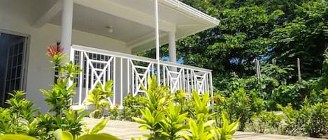 A white building with a covered porch, surrounded by lush greenery and trees.