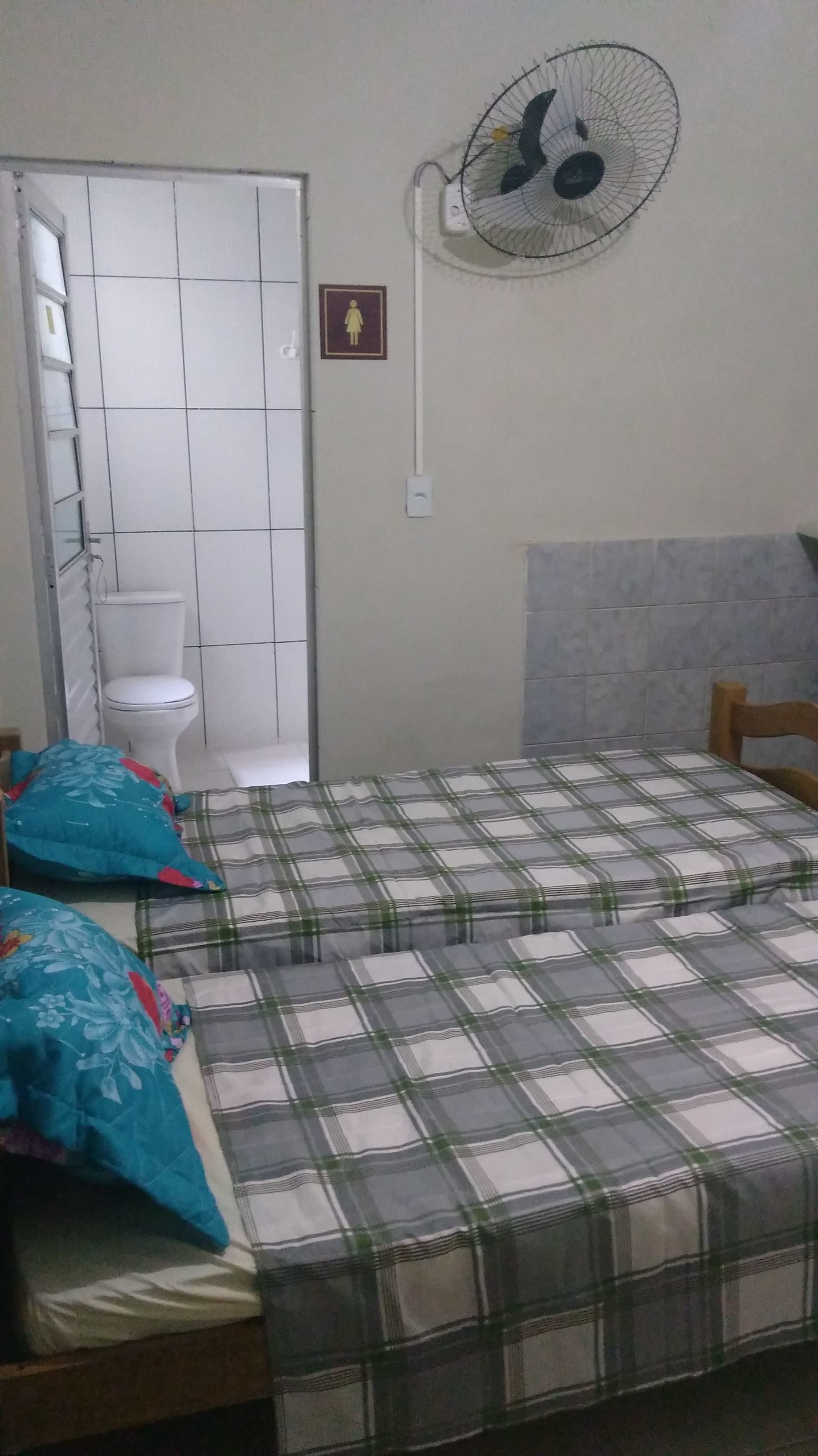 A bedroom with a bed, a fan, a toilet, and a door.