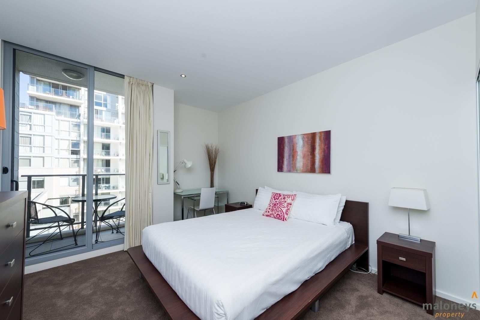 Een moderne hotelkamer met een groot bed, een bureau, een stoel, een kleine tafel en een balkon met stoelen.