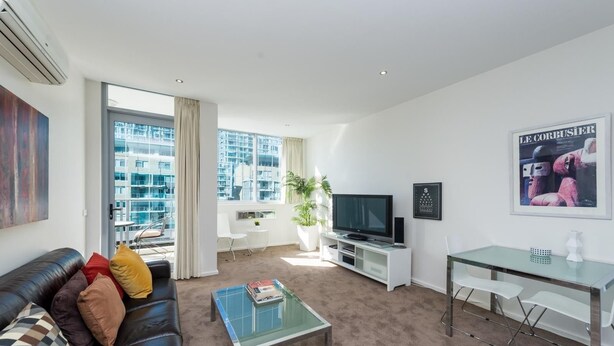 A modern living room with a leather sofa, a glass coffee table, a flat-screen TV, and a dining area with a glass table and chairs.