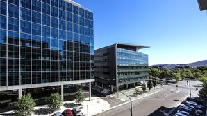 A modern building with a glass facade and a parking lot with several cars.